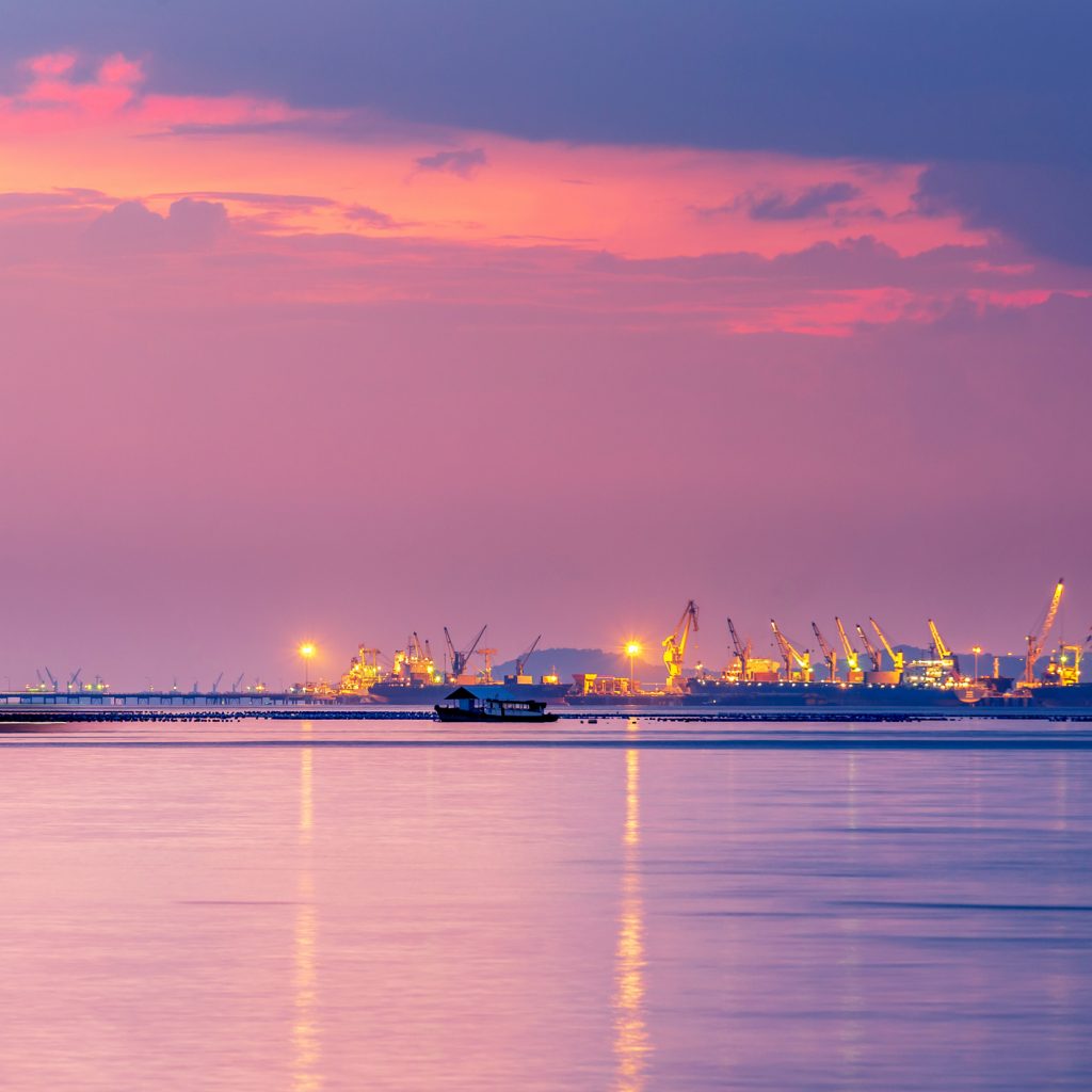 Logistics and transportation of Container Cargo with working crane bridge in shipyard. Cargo shipping and commercial terminal in seaport at sunset. Industrial landscape with gantry cranes in sea port.